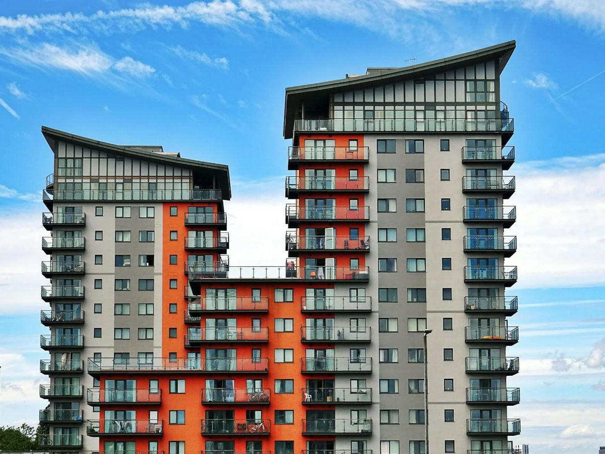 Hoog appartementencomplex met oranje en grijze gevels en glazen balkons onder een blauwe lucht