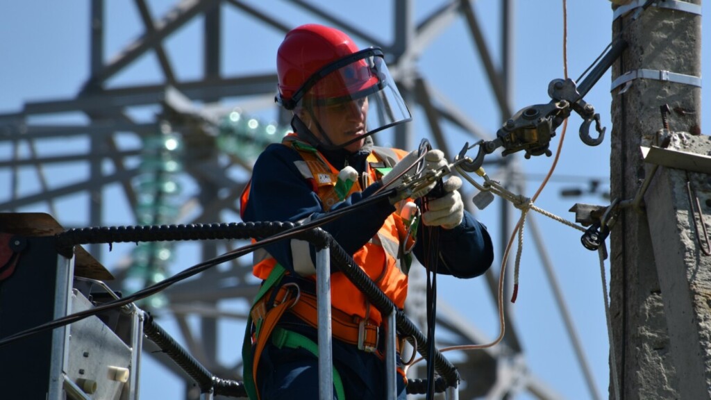 Monteur werkt aan elektriciteitskabels op hoogspanningsmast volgens NEN-normen voor veilige elektrische installaties