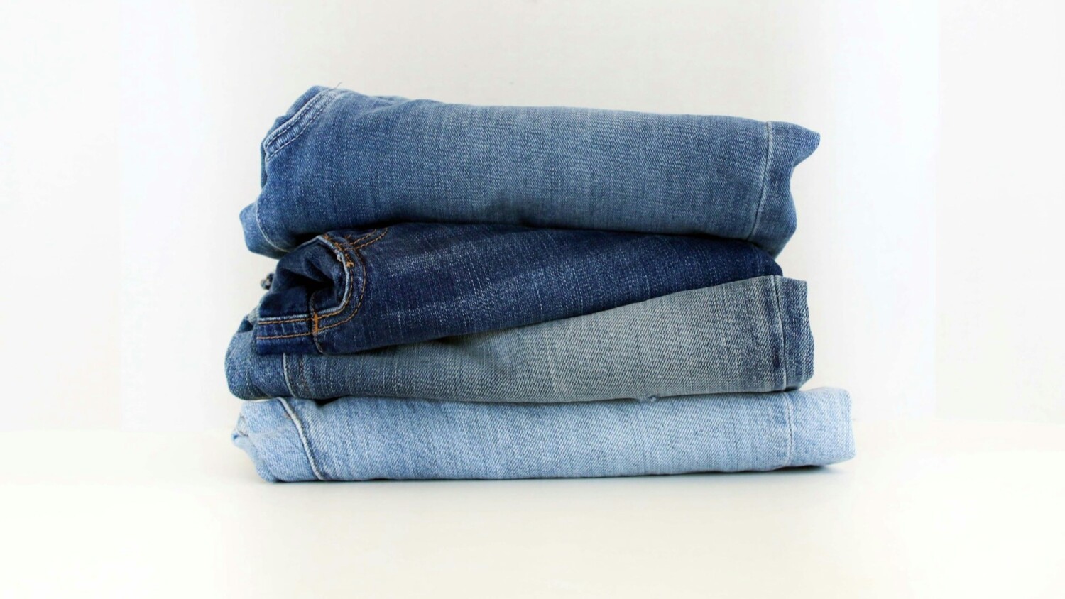 Vier opgevouwen tapered fit jeans in verschillende blauwtinten, gestapeld op een witte ondergrond