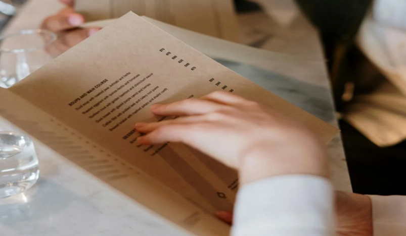 Hand bladert door een minimalistisch restaurantmenu op bruin papier boven een marmeren tafel