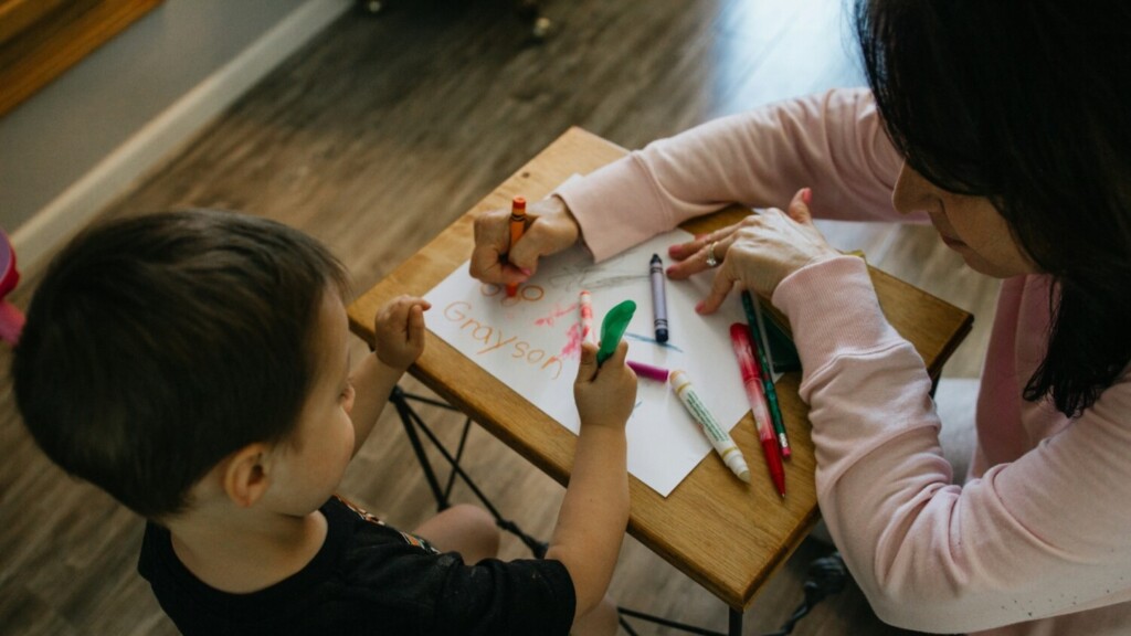Kind tekent met begeleider tijdens buitenschoolse opvang aan tafel met stiften en papier