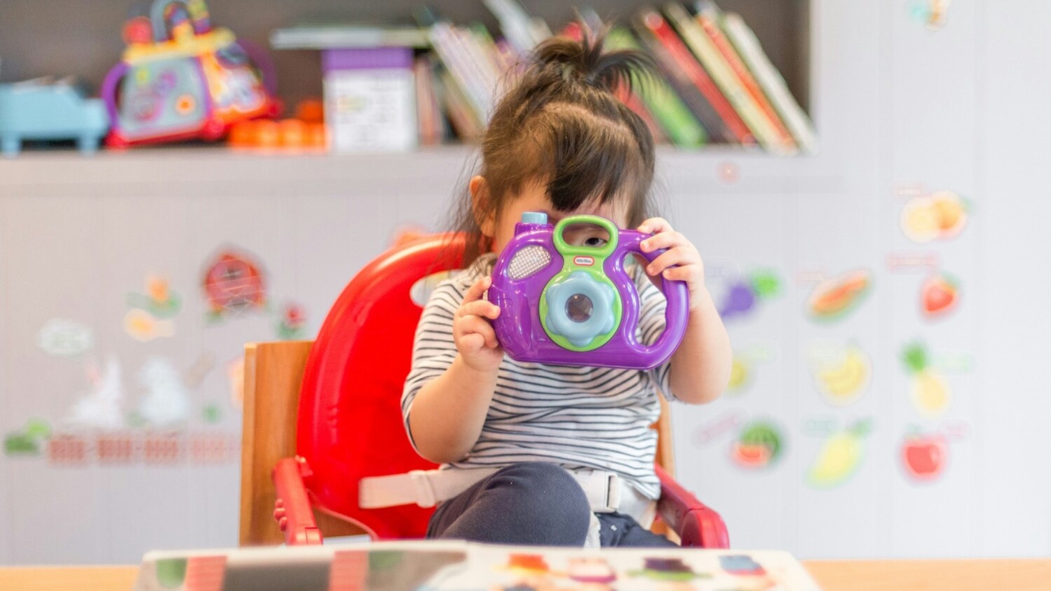 Jong kind speelt met speelgoedcamera tijdens buitenschoolse opvang in een kleurrijke ruimte