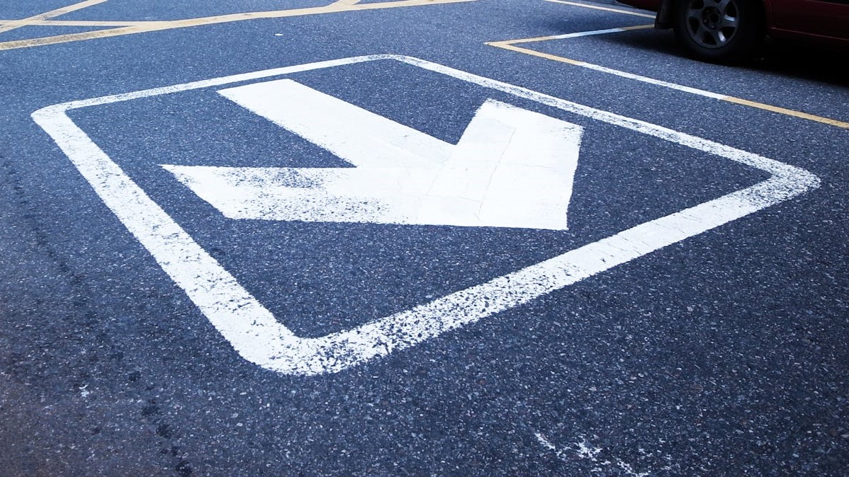 Witte pijl naar rechts-voor op asfalt markeert een laterale rijrichting in een parkeer- of verkeerszone