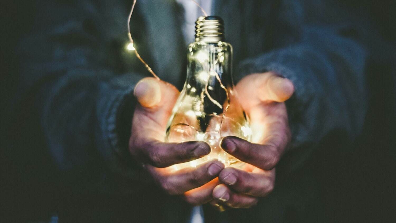 Twee handen houden een lichtgevende gloeilamp vast als metafoor voor innovatief denken en ideeën